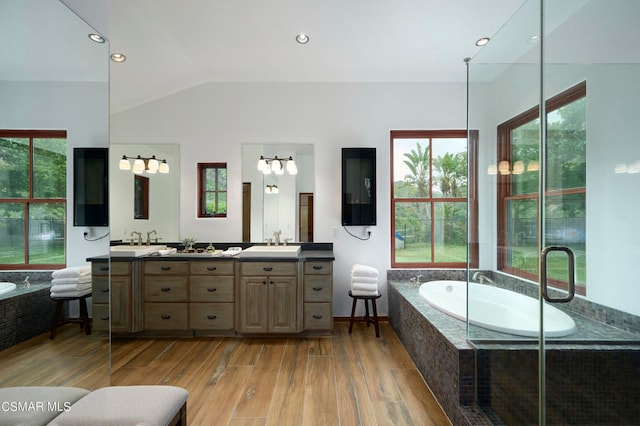 bathroom with vanity, tiled bath, vaulted ceiling, and hardwood / wood-style floors