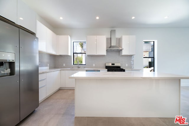 kitchen featuring wall chimney range hood, white cabinets, sink, and appliances with stainless steel finishes