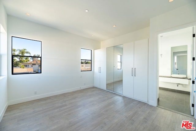 unfurnished bedroom with ensuite bath and light hardwood / wood-style floors