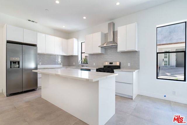 kitchen featuring wall chimney exhaust hood, a kitchen island, appliances with stainless steel finishes, and white cabinets