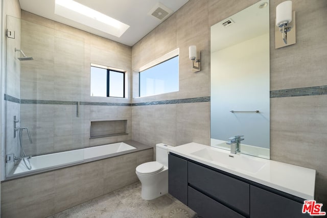 full bathroom with vanity, tiled shower / bath, toilet, and tile walls