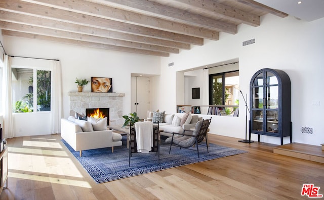 living room featuring a stone fireplace, hardwood / wood-style floors, and beam ceiling