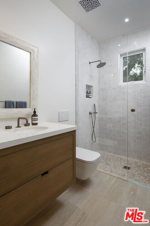 bathroom featuring a tile shower, vanity, wood-type flooring, and toilet