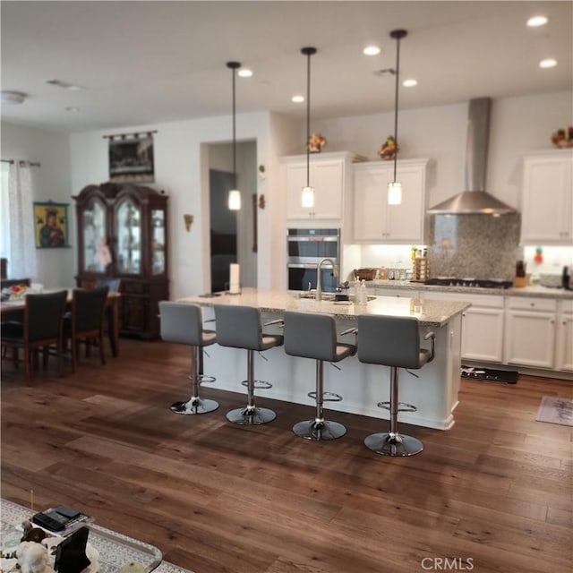 kitchen with dark hardwood / wood-style flooring, decorative light fixtures, wall chimney exhaust hood, and an island with sink