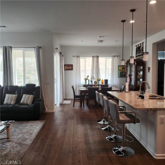 kitchen with sink, hanging light fixtures, light stone countertops, a kitchen bar, and dark hardwood / wood-style flooring