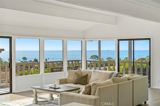 living room featuring lofted ceiling with beams, light hardwood / wood-style flooring, a water view, and plenty of natural light