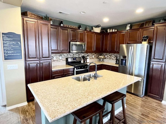 kitchen featuring a kitchen island with sink, a kitchen bar, light wood-type flooring, appliances with stainless steel finishes, and tasteful backsplash