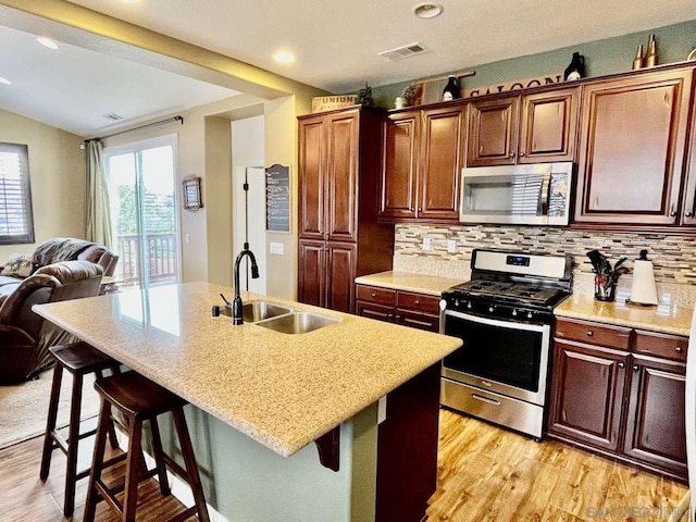 kitchen featuring a kitchen island with sink, a breakfast bar area, sink, light wood-type flooring, and appliances with stainless steel finishes