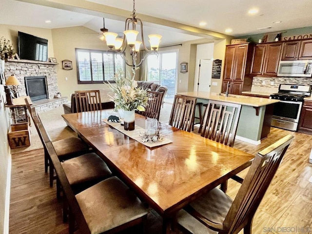 dining space with light hardwood / wood-style flooring, an inviting chandelier, lofted ceiling, and a fireplace