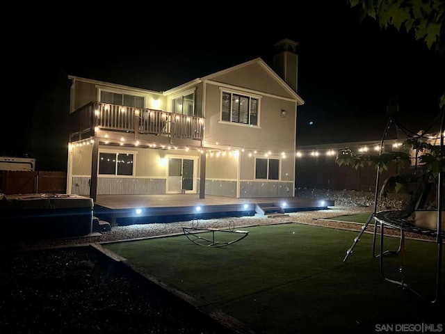 back house at night with a fenced in pool, a trampoline, a lawn, and a balcony