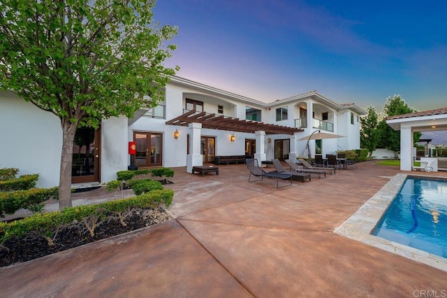 back house at dusk featuring french doors, a balcony, a patio area, and a pergola