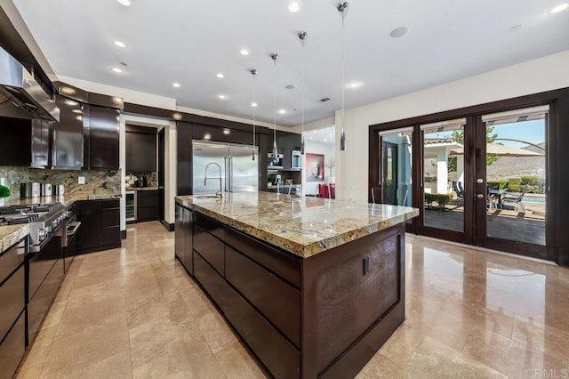 kitchen with a large island with sink, high quality appliances, pendant lighting, light stone countertops, and backsplash