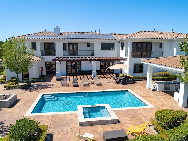 rear view of property featuring solar panels, a balcony, a swimming pool with hot tub, exterior kitchen, and a patio