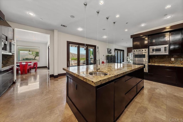 kitchen with french doors, sink, pendant lighting, stainless steel appliances, and a kitchen island with sink