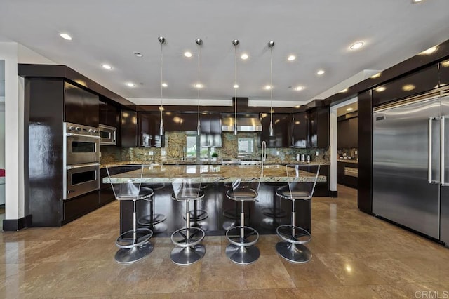 kitchen featuring a large island, built in appliances, light stone countertops, and hanging light fixtures