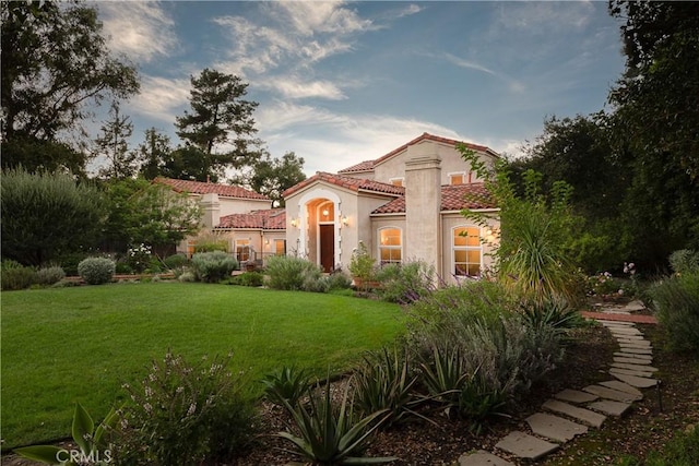 mediterranean / spanish home featuring a front yard, a tiled roof, and stucco siding