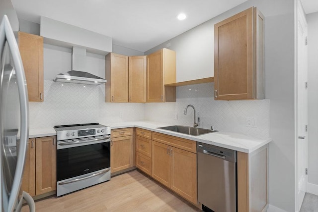 kitchen featuring wall chimney range hood, backsplash, appliances with stainless steel finishes, light hardwood / wood-style floors, and sink