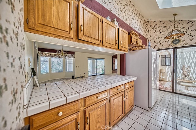 kitchen featuring white refrigerator, tile countertops, hanging light fixtures, an inviting chandelier, and light tile patterned floors