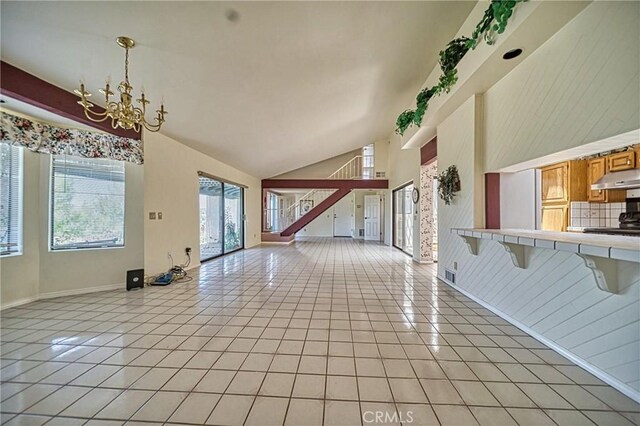 unfurnished living room featuring high vaulted ceiling, light tile patterned floors, a chandelier, and wood walls