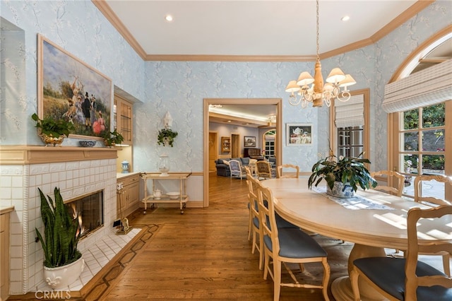 dining space with a tile fireplace, light hardwood / wood-style floors, a chandelier, and ornamental molding