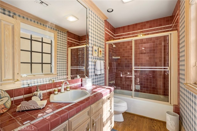 full bathroom with vanity, toilet, wood-type flooring, and bath / shower combo with glass door