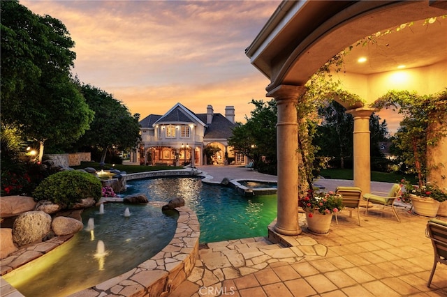 pool at dusk featuring an in ground hot tub, pool water feature, and a patio area