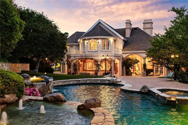 pool at dusk featuring pool water feature and an in ground hot tub