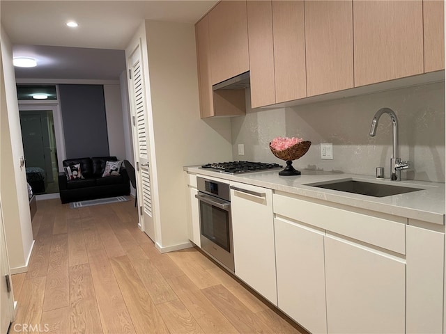 kitchen with sink, appliances with stainless steel finishes, exhaust hood, and light wood-type flooring