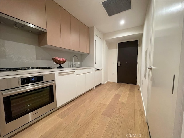 kitchen featuring white gas stovetop, light hardwood / wood-style flooring, white cabinetry, and oven