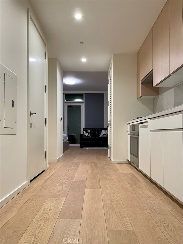 kitchen with light hardwood / wood-style floors, electric panel, exhaust hood, and stainless steel oven