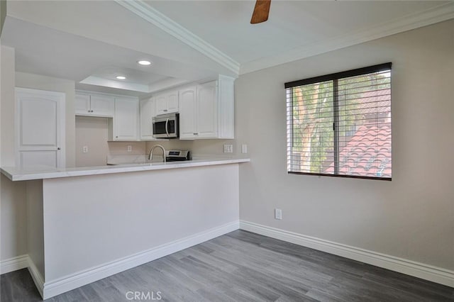 kitchen with ceiling fan, dark wood-type flooring, kitchen peninsula, crown molding, and white cabinets