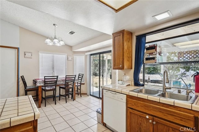 kitchen featuring a textured ceiling, white dishwasher, sink, decorative light fixtures, and tile counters