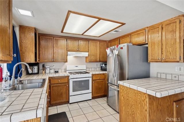 kitchen featuring white range, sink, light tile patterned floors, tile countertops, and stainless steel refrigerator