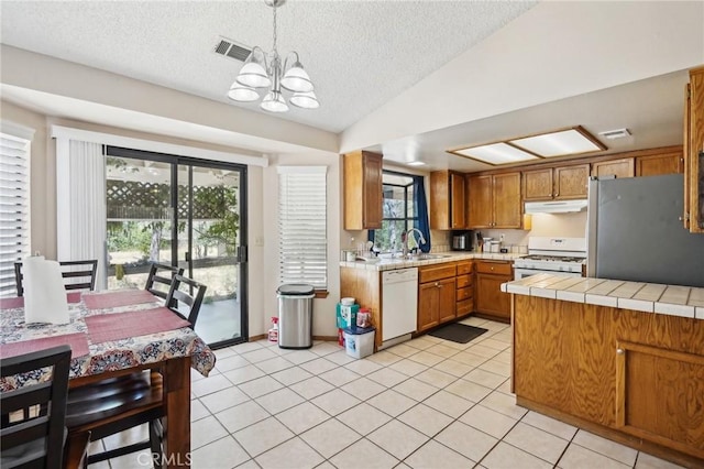 kitchen featuring a wealth of natural light, white appliances, vaulted ceiling, and hanging light fixtures