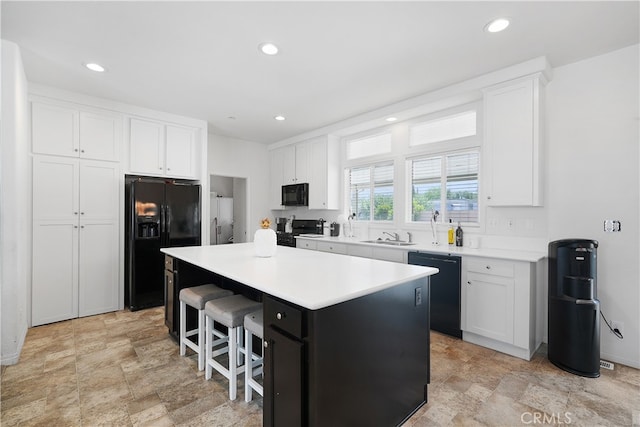 kitchen with a breakfast bar, white cabinetry, black appliances, and a center island