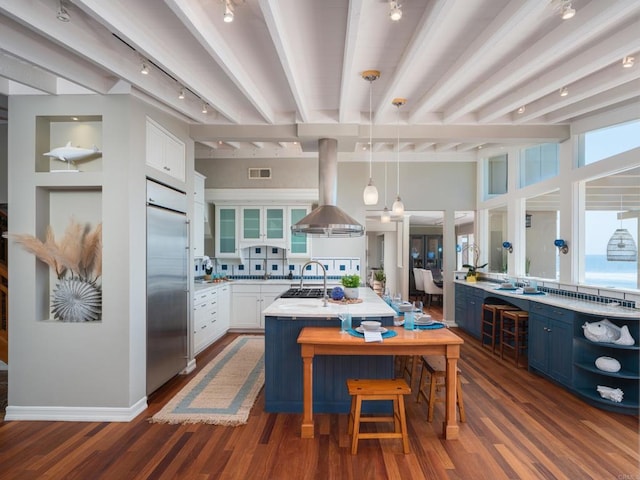 kitchen with white cabinets, appliances with stainless steel finishes, island exhaust hood, an island with sink, and blue cabinetry