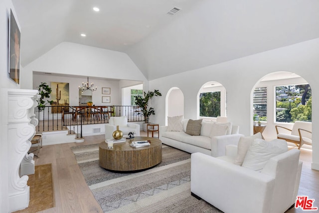 living room featuring light hardwood / wood-style flooring, high vaulted ceiling, a notable chandelier, and plenty of natural light