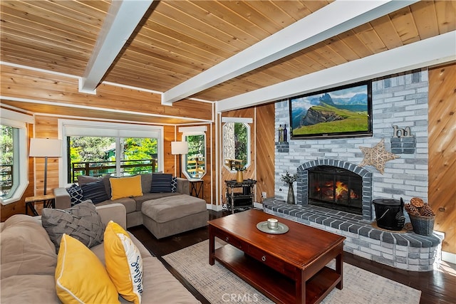 living room featuring beam ceiling, wooden walls, a brick fireplace, and a healthy amount of sunlight