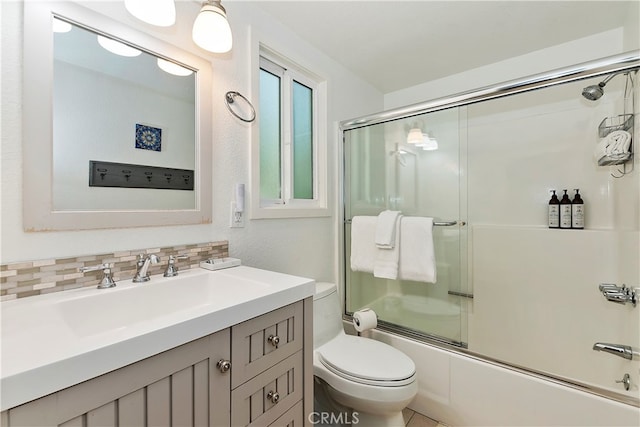 full bathroom with bath / shower combo with glass door, decorative backsplash, toilet, and vanity