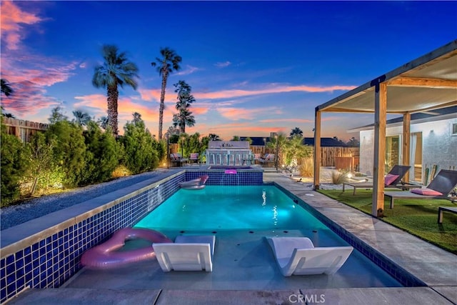 pool at dusk with a fenced backyard and a pool with connected hot tub