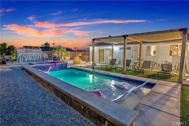 pool at dusk with a pool with connected hot tub, fence, and a patio