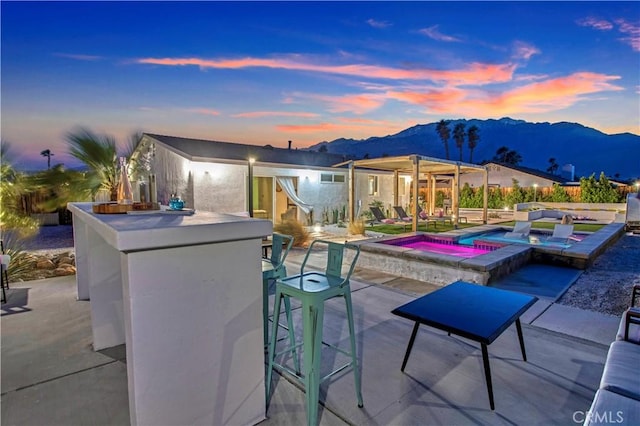 exterior space with a pool with connected hot tub, a mountain view, outdoor dry bar, and a patio