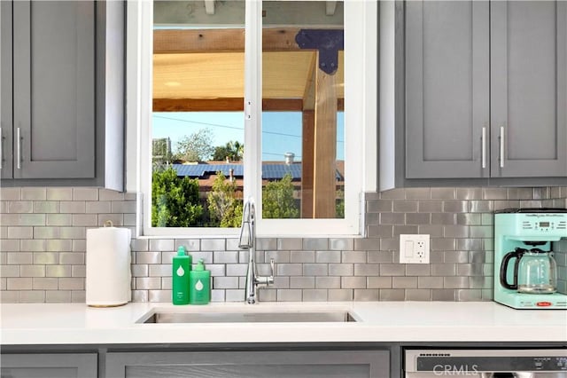 room details with dishwasher, backsplash, gray cabinets, light countertops, and a sink