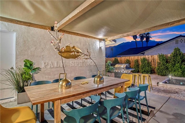 patio terrace at dusk featuring fence, outdoor dining area, and area for grilling