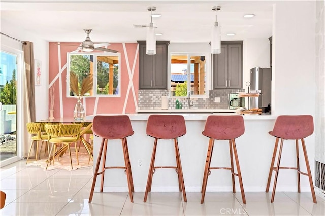 kitchen featuring a kitchen breakfast bar, light countertops, gray cabinetry, pendant lighting, and backsplash