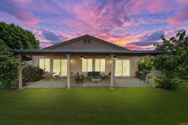 back house at dusk featuring a yard, a patio, and ceiling fan