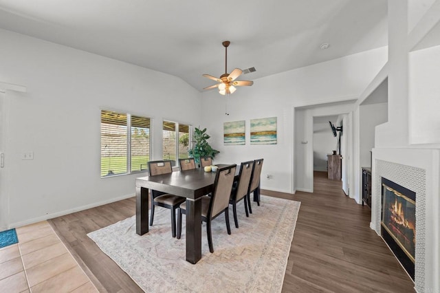 dining area with ceiling fan, hardwood / wood-style flooring, vaulted ceiling, and a fireplace