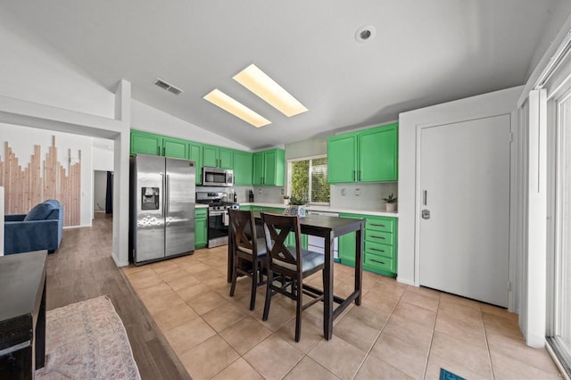 kitchen featuring tasteful backsplash, green cabinets, stainless steel appliances, vaulted ceiling, and light hardwood / wood-style flooring