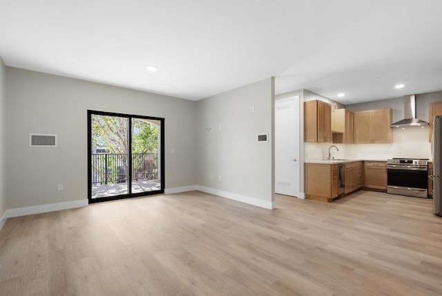 kitchen with light wood-type flooring, wall chimney exhaust hood, sink, and stainless steel range