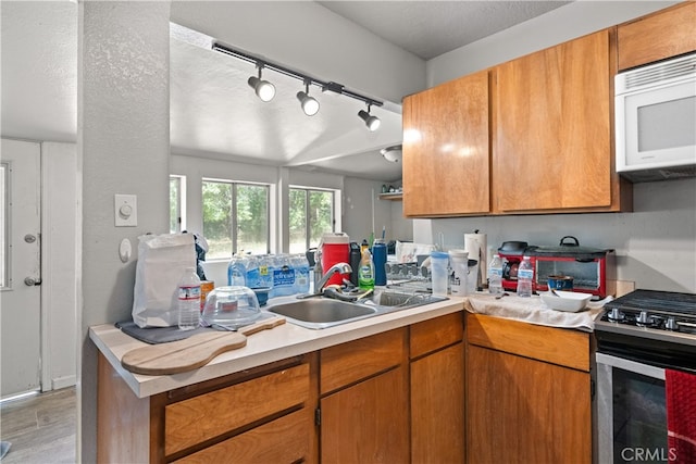 kitchen featuring kitchen peninsula, rail lighting, stainless steel stove, light hardwood / wood-style floors, and sink